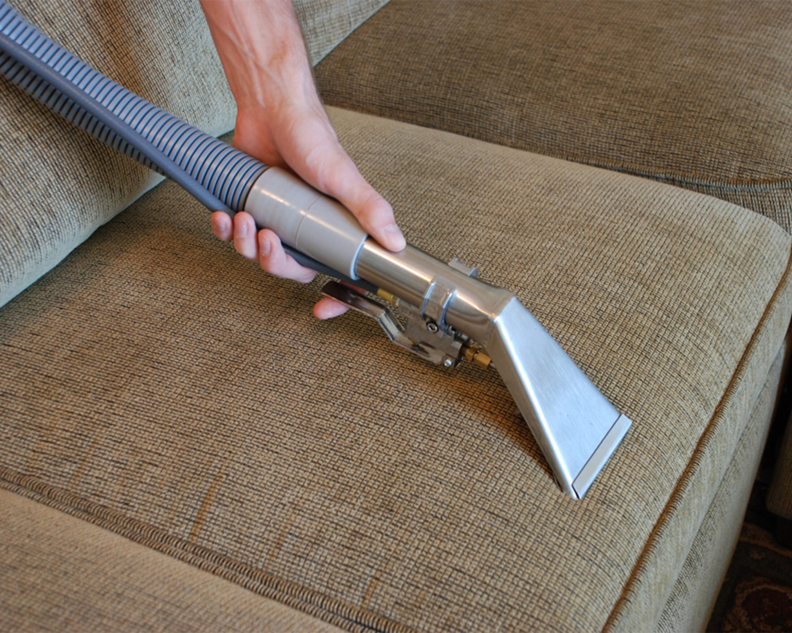 Hand using vacuum tool on sofa fabric